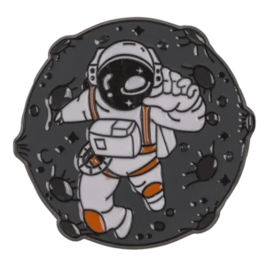 Kosmonauto pin'as kosmose – astronautas baltu skafandru su oranžinėmis detalėmis tarp asteroidų tamsus emalio ženkliukas