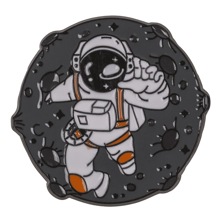 Kosmonauto pin'as kosmose – astronautas baltu skafandru su oranžinėmis detalėmis tarp asteroidų tamsus emalio ženkliukas